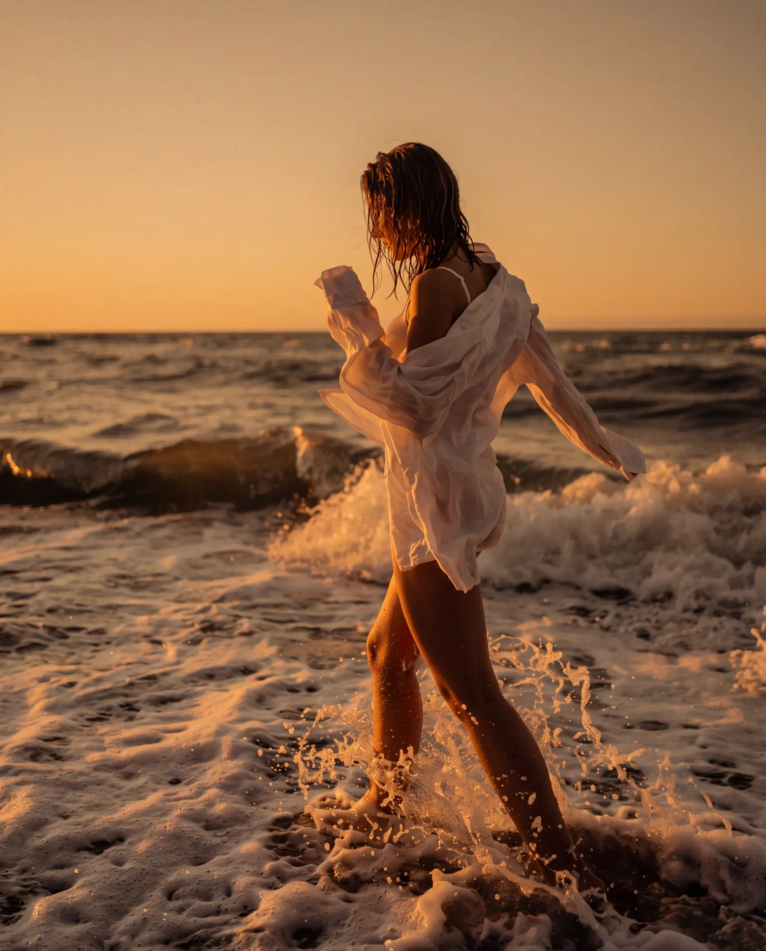 Woman standing in sunlit coastal shallows at golden hour, looking down at the water in quiet reflection.